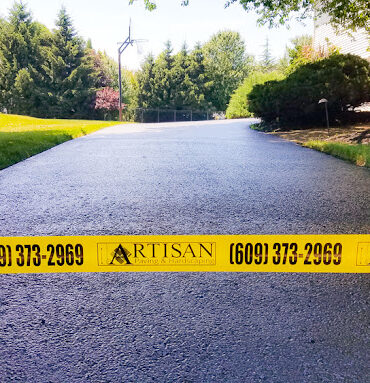 Freshly sealcoated driveway with Artisan Outdoor Contractors custom caution tape, completed by a local asphalt maintenance company in Bucks County, specializing in trusted driveway sealing, professional sealcoating, and affordable asphalt repair services in PA and NJ.