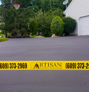 Freshly sealcoated driveway with Artisan Outdoor Contractors custom caution tape, completed by a local asphalt maintenance company in Bucks County, specializing in trusted driveway sealing and affordable asphalt repair services in NJ and PA.