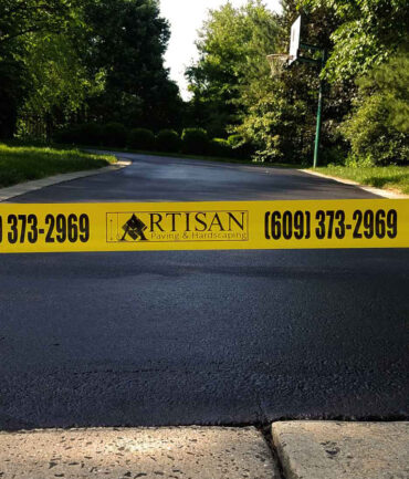 Freshly sealcoated driveway with pothole repairs and crack filling, secured with Artisan Outdoor Contractors' custom caution tape in Bucks County, PA.