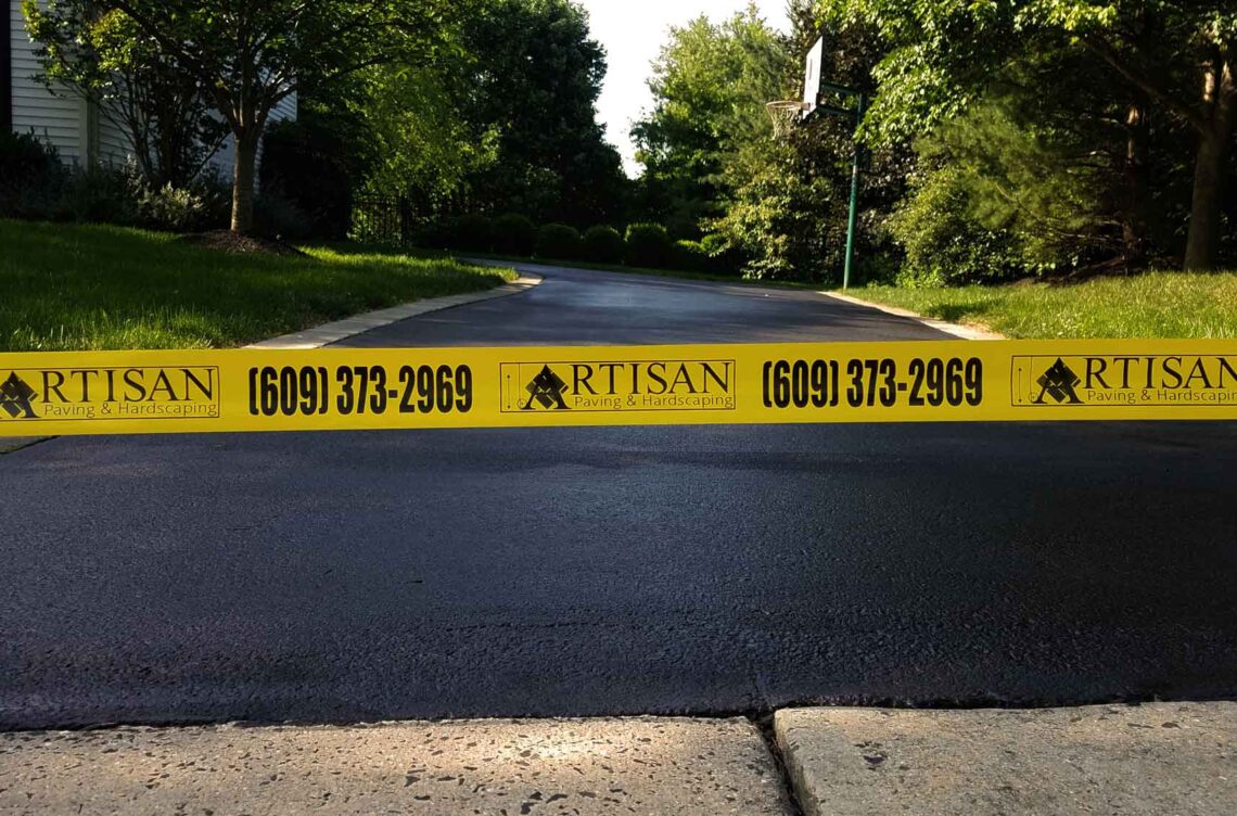 Freshly sealcoated driveway with pothole repairs and crack filling, secured with Artisan Outdoor Contractors' custom caution tape in Bucks County, PA.