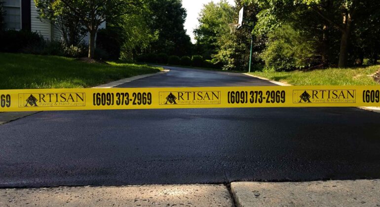 Freshly sealcoated driveway with pothole repairs and crack filling, secured with Artisan Outdoor Contractors' custom caution tape in Bucks County, PA.