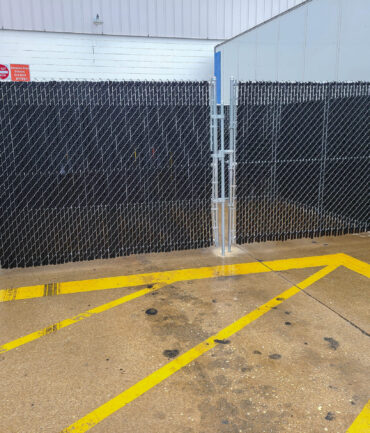 A secure chain link fence enclosure installed by Artisan Outdoor Contractors for an industrial facility. Featuring black privacy slats and a double-gate entry, this enclosure provides both security and functionality for restricted access areas.