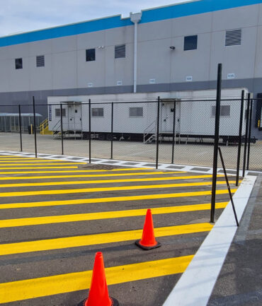 A completed project by Artisan Outdoor Contractors, featuring freshly applied yellow and white line striping and a newly installed chain link fence for an industrial facility. This job enhances safety, organization, and traffic flow within the site while maintaining a professional and durable finish.